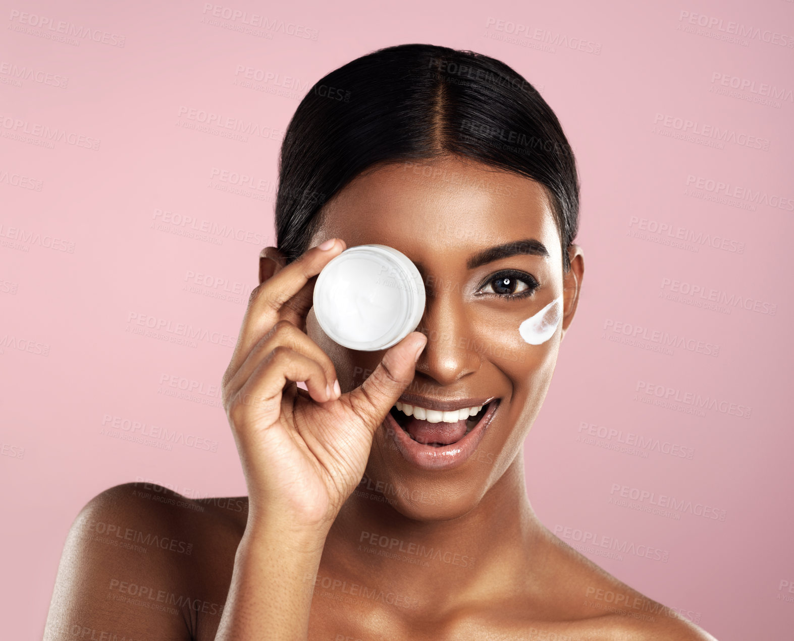 Buy stock photo Studio shot of a beautiful young woman posing with moisturizer on her face against a pink background