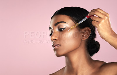 Buy stock photo Studio shot of a beautiful young woman applying essential oil to her face with a dropper posing against a pink background