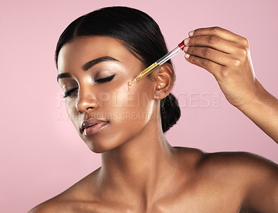 Buy stock photo Studio shot of a beautiful young woman applying essential oil to her face with a dropper posing against a pink background