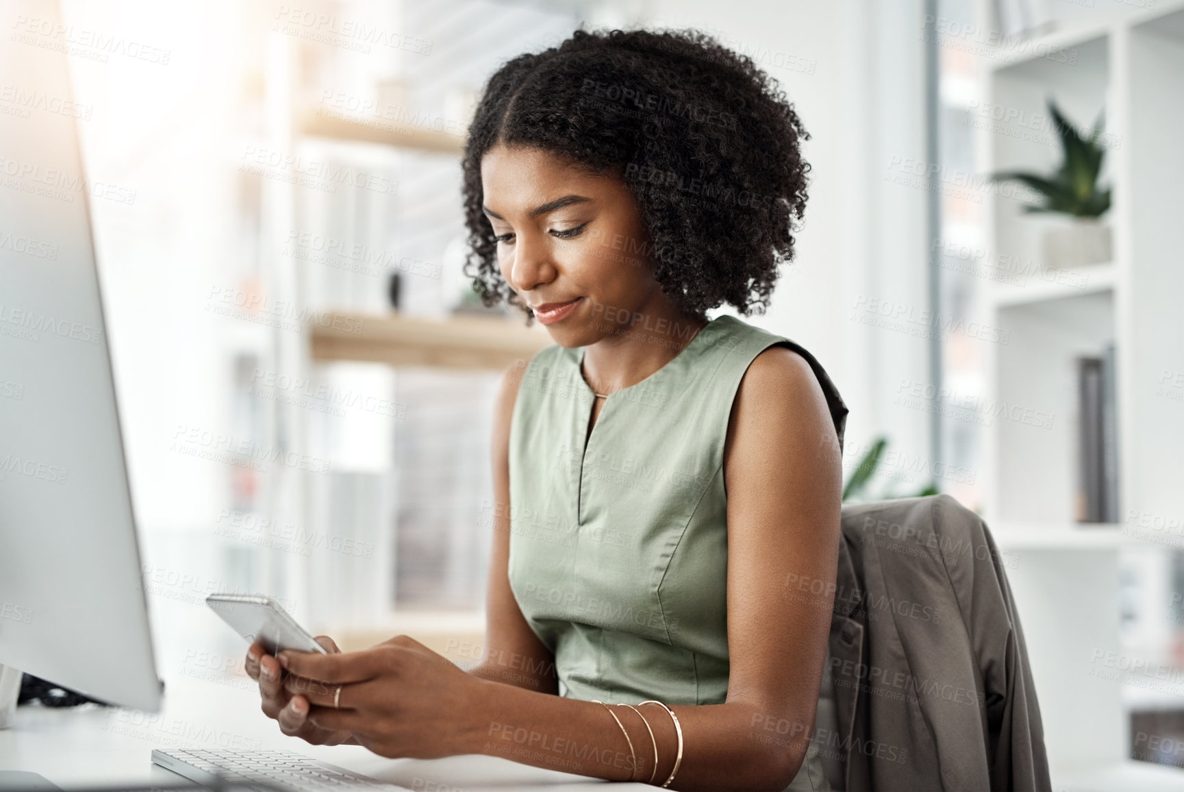 Buy stock photo Shot of a young businesswoman using a mobile phone at her desk in a modern office