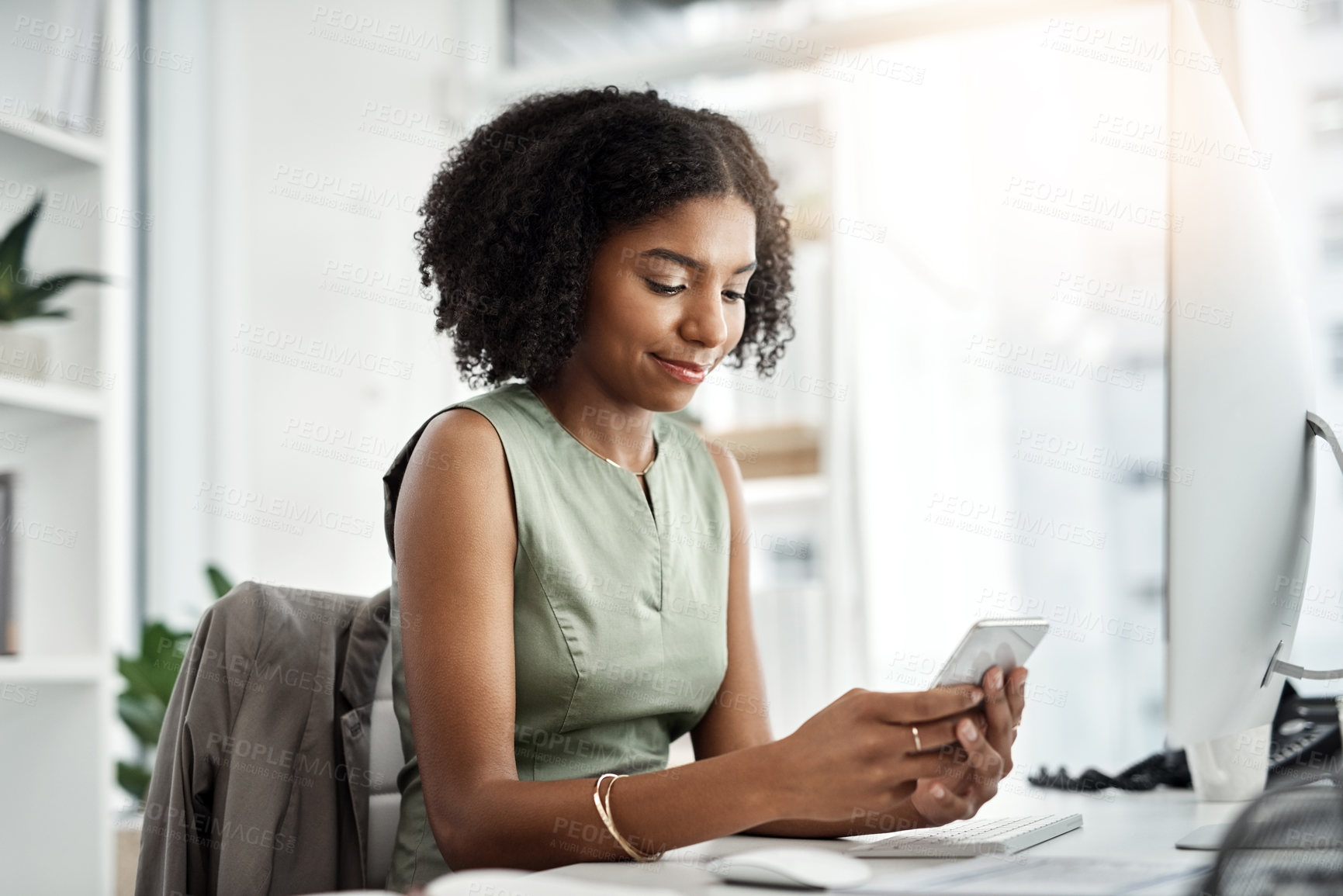 Buy stock photo Shot of a young businesswoman using a mobile phone at her desk in a modern office