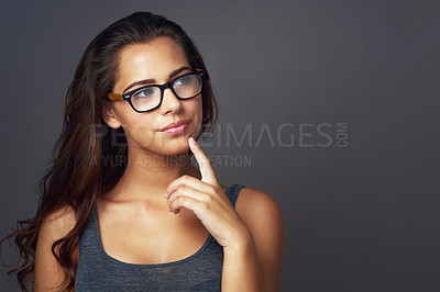 Buy stock photo Studio shot of an attractive young woman looking thoughtful while wearing glasses against a grey background