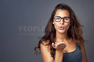 Buy stock photo Studio shot of an attractive young woman blowing a kiss while posing against a grey background