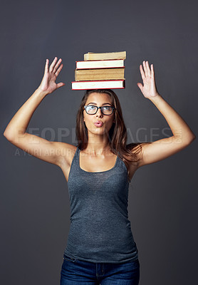 Buy stock photo Studio shot of a young woman balancing a pile of books on her head against a grey background