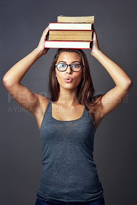 Buy stock photo Studio portrait of a young woman balancing a pile of books on her head against a grey background