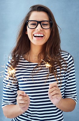 Buy stock photo Portrait, woman and happy in studio with sparklers for celebration isolated on blue background with light. Glasses, smile and fun event with birthday or new year with glow, vision and fireworks.