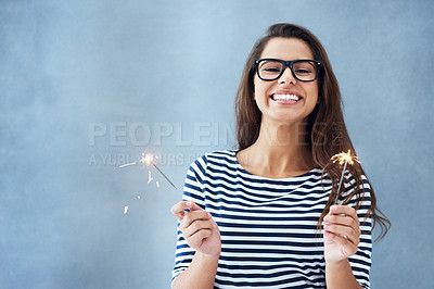 Buy stock photo Portrait, happiness and woman in studio with sparklers isolated on blue background for celebration. Glasses, light and fun birthday event or new year with glow, vision and fireworks with confidence.