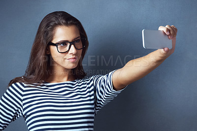 Buy stock photo Studio shot of an attractive young woman taking a selfie against a dark background