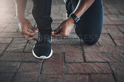 Buy stock photo Cropped shot of an unrecognizable young man tying his laces while exercising outside