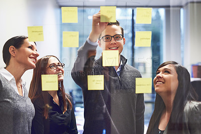 Buy stock photo Cropped shot of a group of businesspeople brainstorming on a glass wall in an office