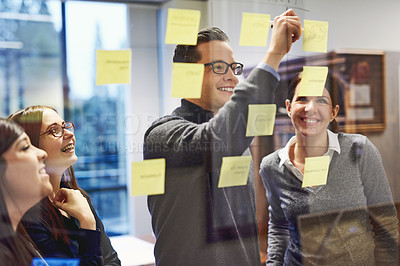 Buy stock photo Cropped shot of a group of businesspeople brainstorming on a glass wall in an office