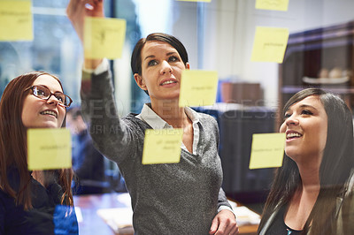 Buy stock photo Cropped shot of a group of businesswomen brainstorming on a glass wall in an office