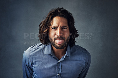 Buy stock photo Studio portrait of a handsome young man sticking his tongue out while posing against a grey background