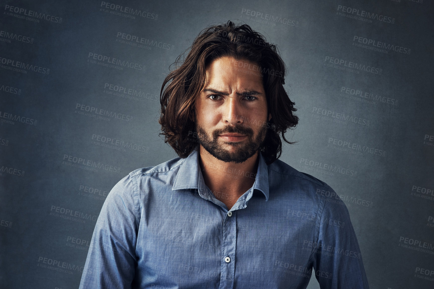 Buy stock photo Serious man, portrait and fashion with hairstyle, beard or frown for attitude on a gray studio background. Handsome male person or young model with facial expression, aggression or casual tshirt 