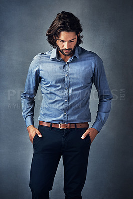 Buy stock photo Studio shot of a handsome young man standing with his hands in his pockets against a grey background