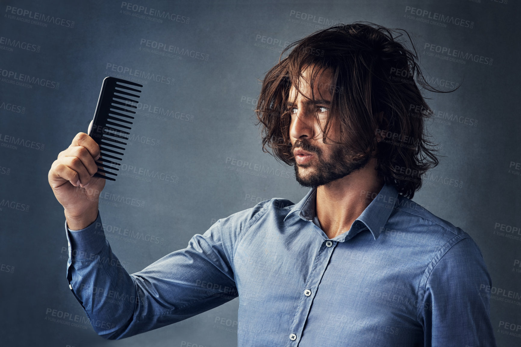 Buy stock photo Studio shot of a handsome young man looking at his comb while brushing his hair against a grey background