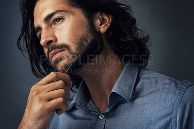 Buy stock photo Studio shot of a handsome young man combing his beard against a grey background