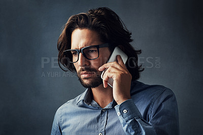 Buy stock photo Studio shot of a handsome young man talking on his cellphone while standing against a grey background
