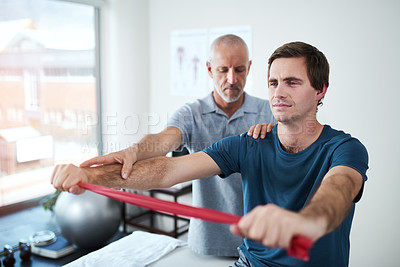 Buy stock photo Cropped shot of a handsome mature male physiotherapist helping a patient stretch with resistance bands