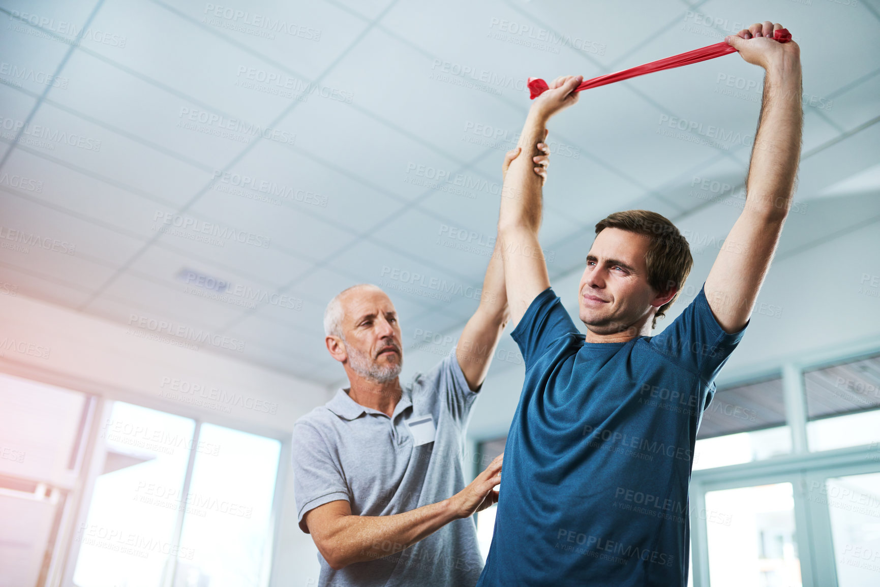 Buy stock photo Low angle shot of a handsome mature male physiotherapist helping a patient stretch with resistance bands