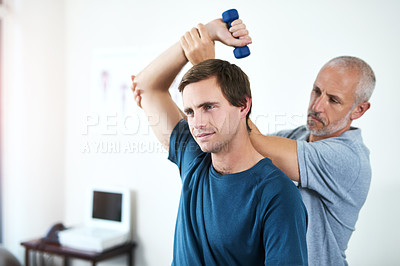 Buy stock photo Cropped shot of a handsome mature male physiotherapist helping a patient work through his recovery with weights