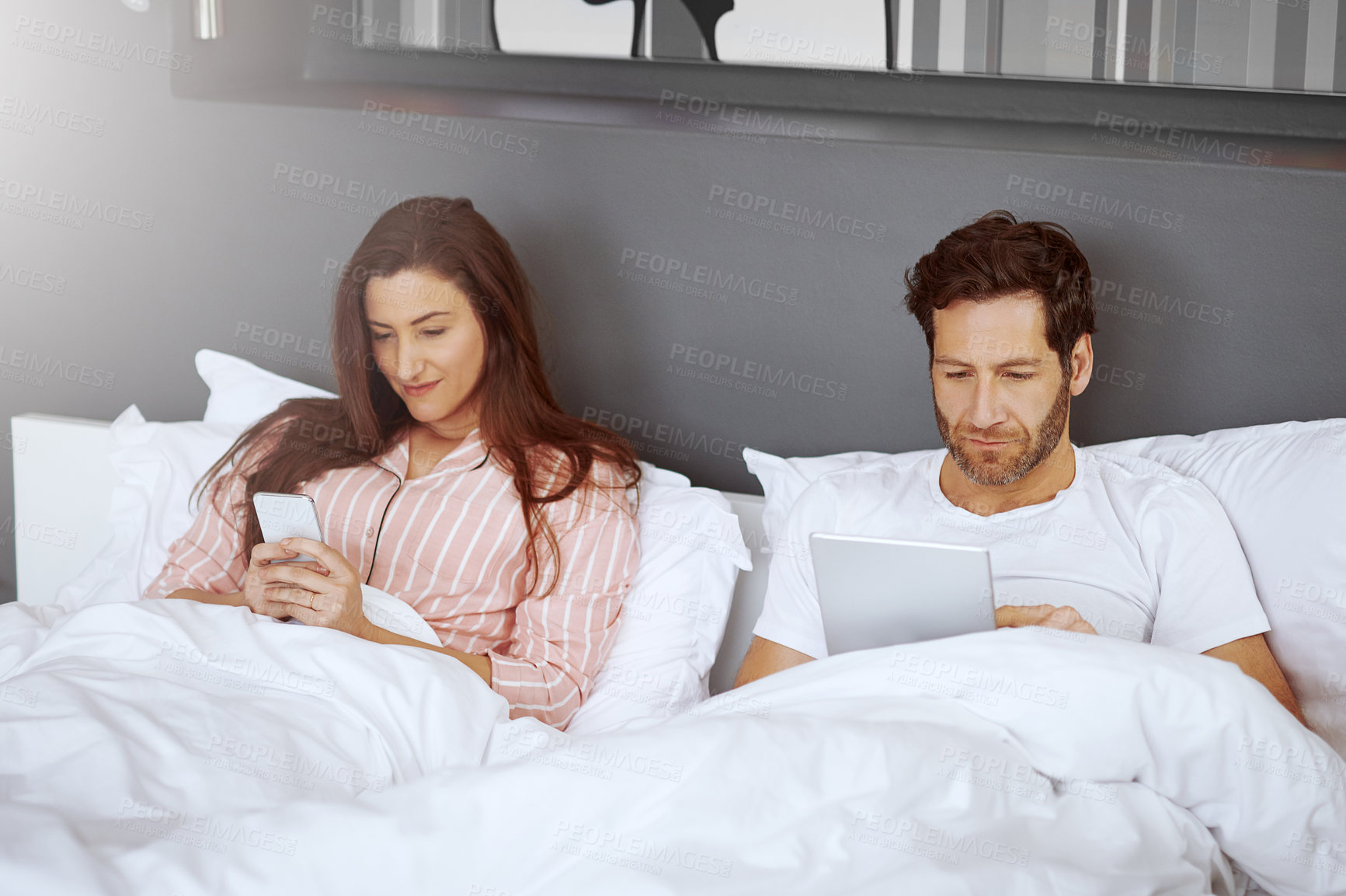 Buy stock photo Shot of a couple using their wireless devices while lying in bed