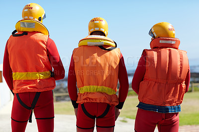Buy stock photo Rearview shot of three unrecognizable lifeguards keeping their eyes on the ocean and the horizon