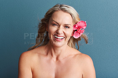 Buy stock photo Studio portrait of an attractive mature woman posing with a flower in her hair against a grey background