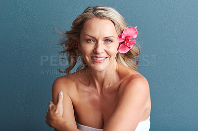 Buy stock photo Studio portrait of an attractive mature woman posing with a flower in her hair against a grey background