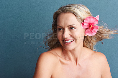 Buy stock photo Studio shot of an attractive mature woman posing with a flower in her hair against a grey background