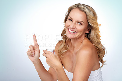 Buy stock photo Studio portrait of an attractive mature woman applying moisturizer against a grey background