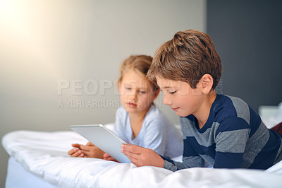 Buy stock photo Cropped shot of an adorable little girl and boy using a tablet together while chilling on the bed at home