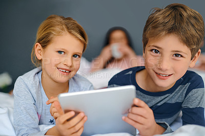 Buy stock photo Shot of an adorable little girl and boy using a tablet together while their parents are chilling in bed at home