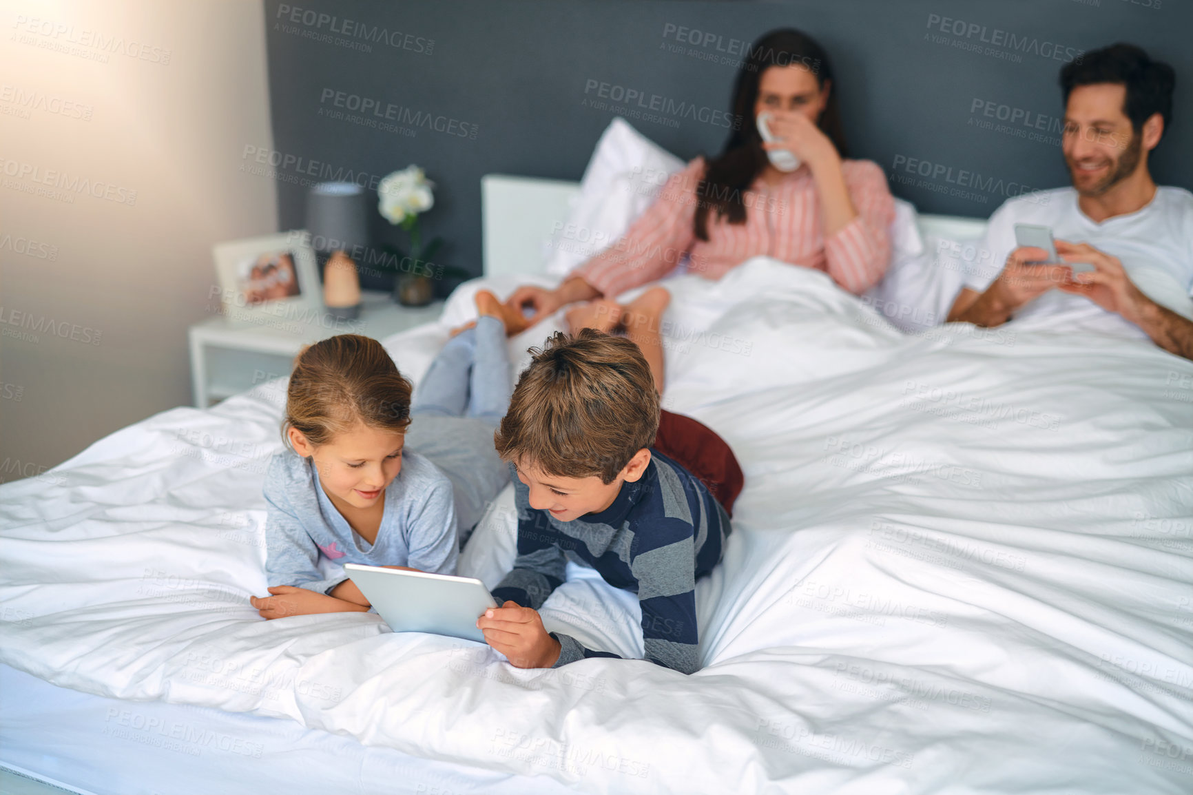 Buy stock photo Shot of an adorable little girl and boy using a tablet together while their parents are chilling in bed at home