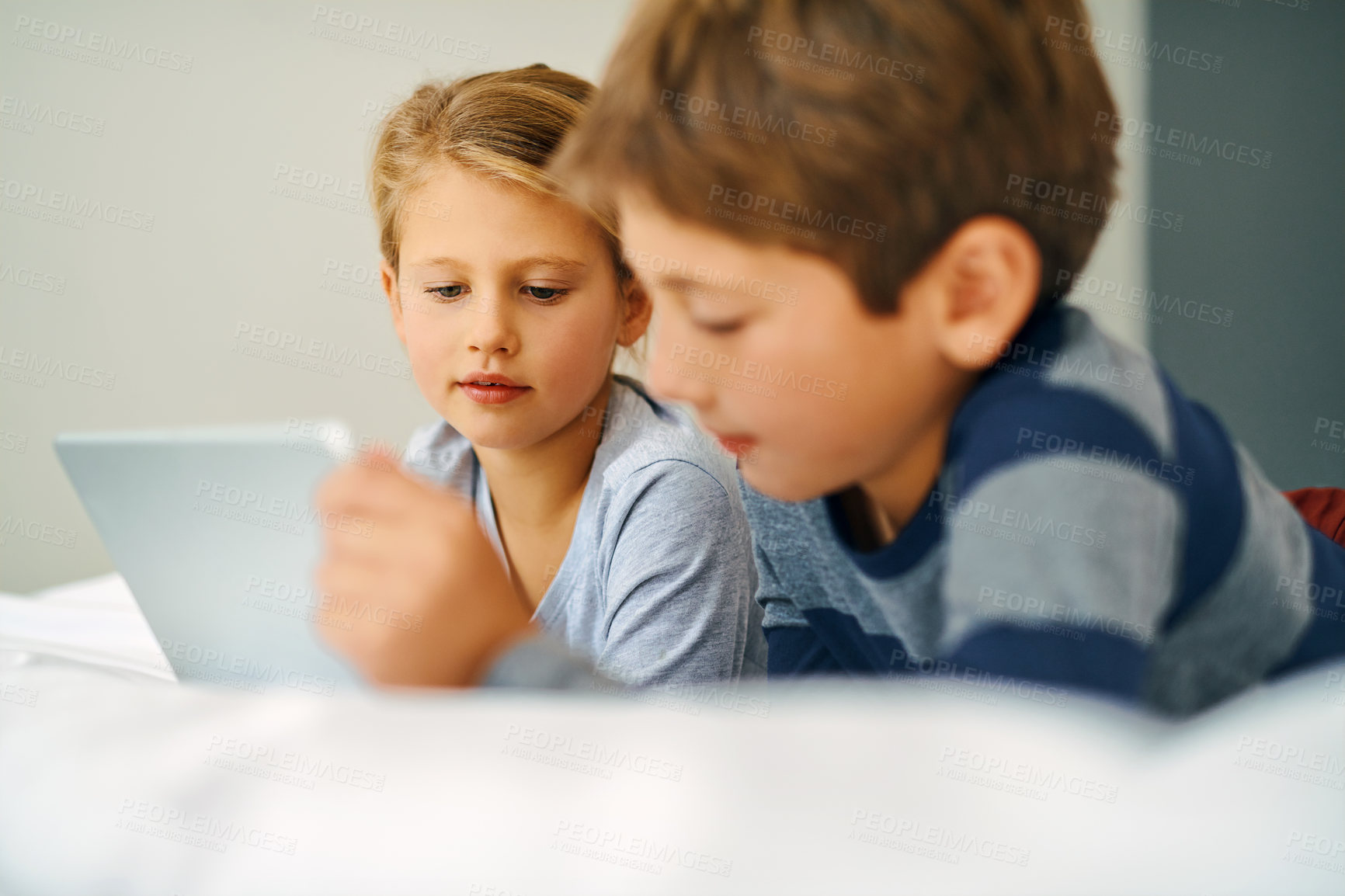 Buy stock photo Cropped shot of an adorable little girl and boy using a tablet together while chilling on the bed at home