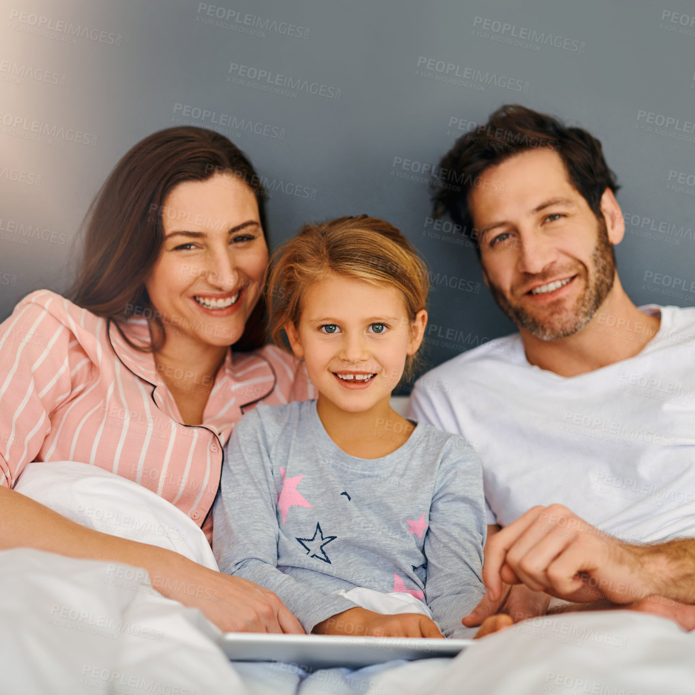 Buy stock photo Cropped shot of a young family using a tablet while chilling in bed together at home