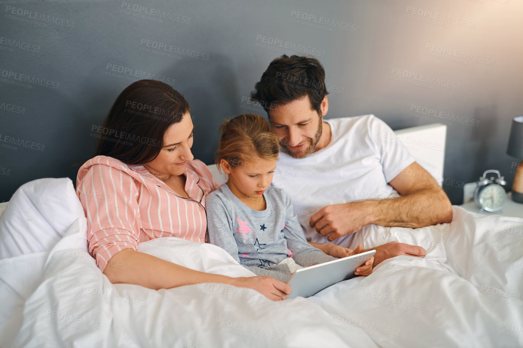 Buy stock photo Parents, relax and daughter in bed for movie, bonding and playing games together on app with smile. Family, girl and technology in apartment for streaming film, support and cartoon with development