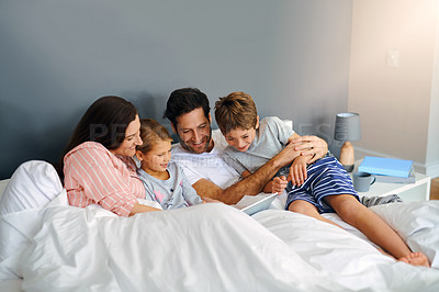 Buy stock photo Cropped shot of a young family using a tablet while chilling in bed together at home