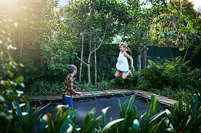 Buy stock photo Shot of an adorable little boy and girl jumping on a trampoline in the backyard at home
