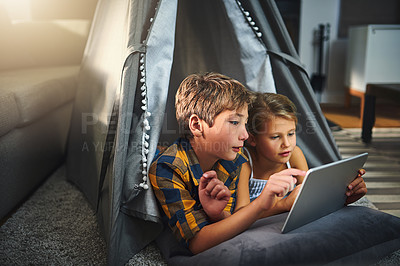 Buy stock photo Cropped shot of an adorable little boy and girl using a tablet together while chilling in a homemade tent in the living room at home