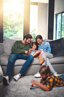 Buy stock photo Cropped shot of a mother, father and their daughter using a tablet together on the sofa while their son plays on the floor in the living room at home