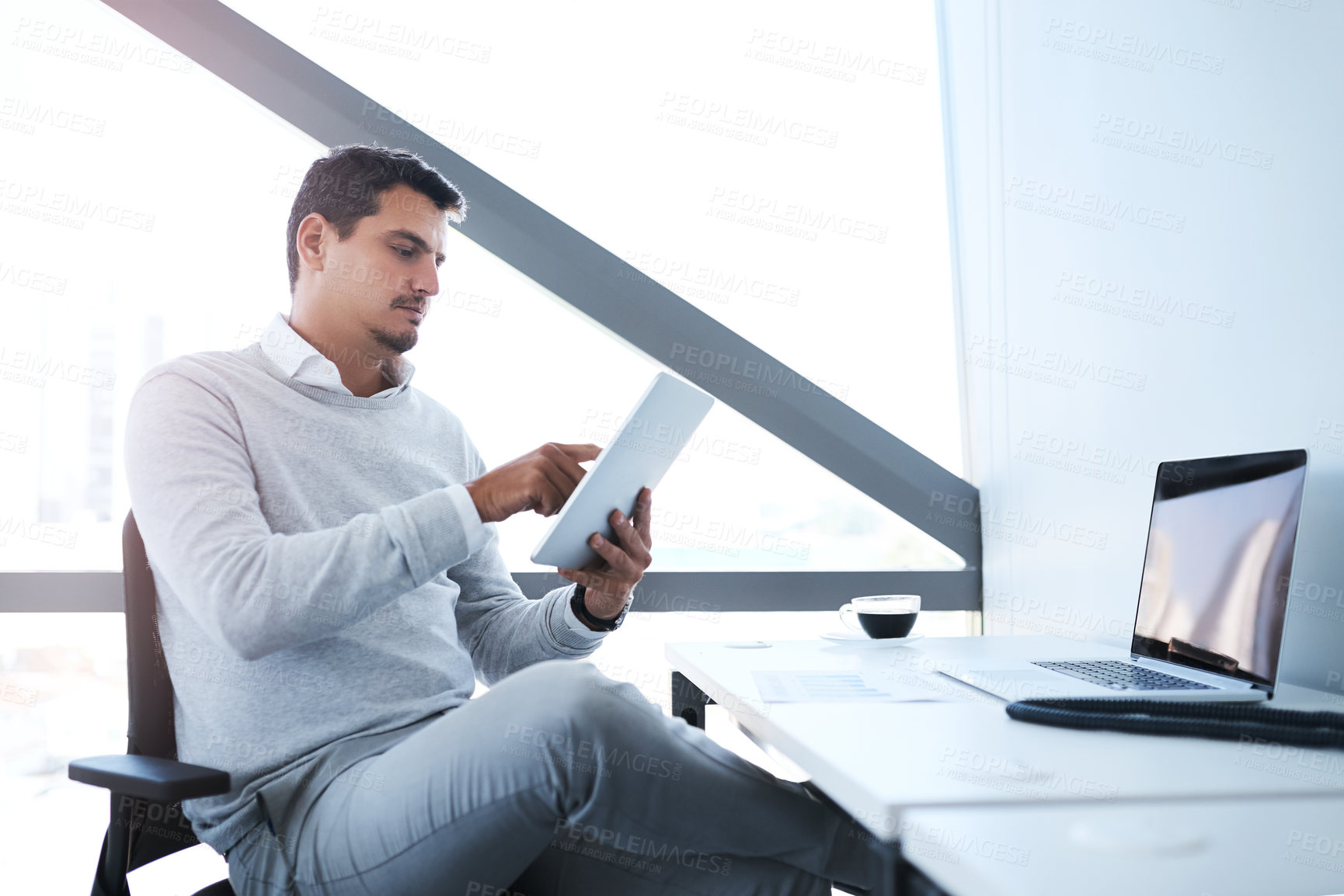 Buy stock photo Shot of a young businessman working on a digital tablet in an office