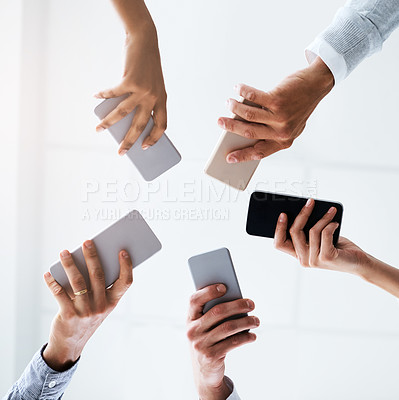 Buy stock photo Low angle shot of a group of businesspeople using their cellphones in synchronicity in an office