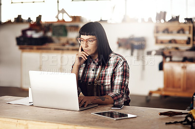 Buy stock photo Cropped shot of an attractive young woman looking thoughtful while working on her laptop in her creative workshop