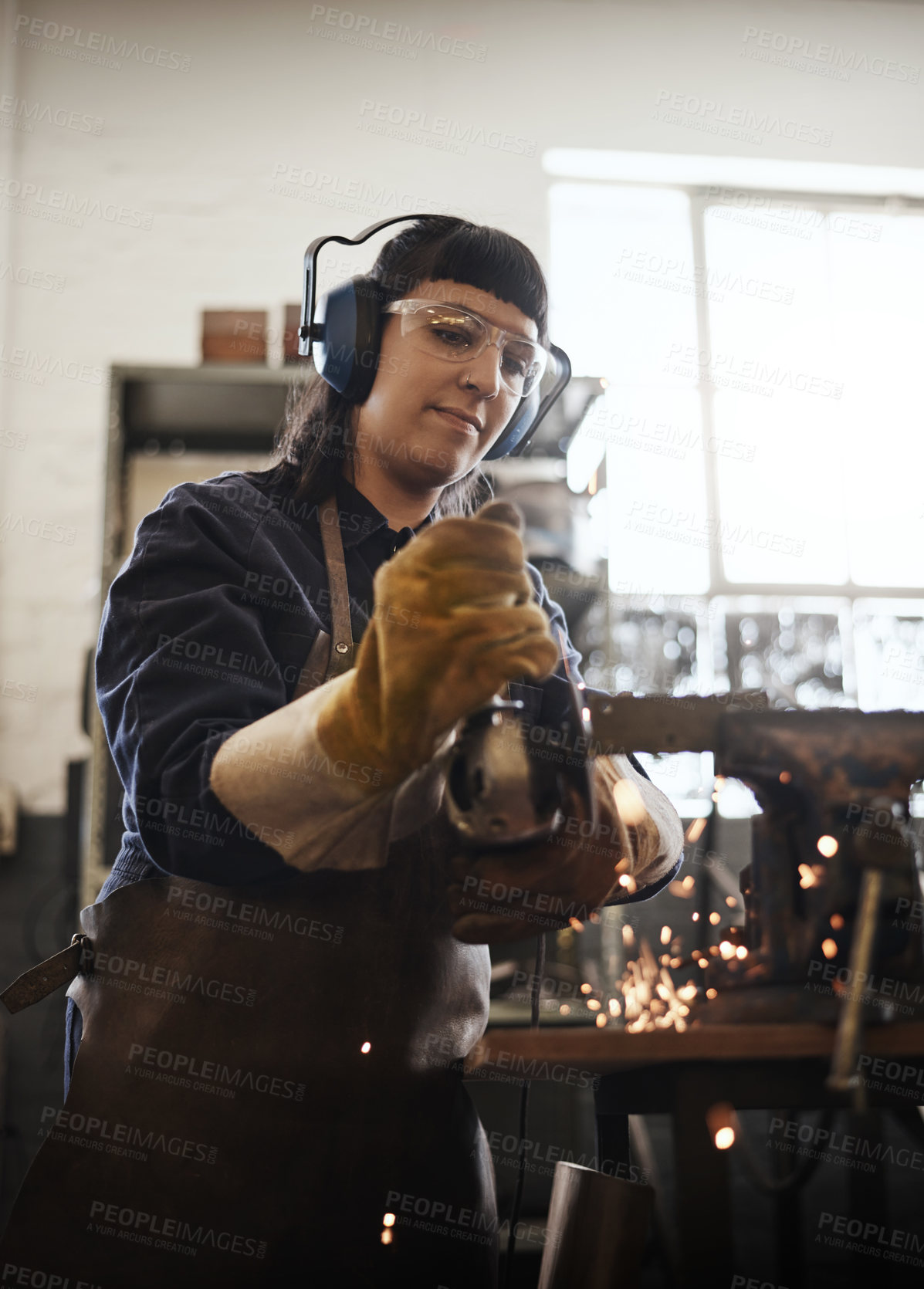 Buy stock photo Cropped shot of an attractive young female artisan using an angle grinder in her workshop