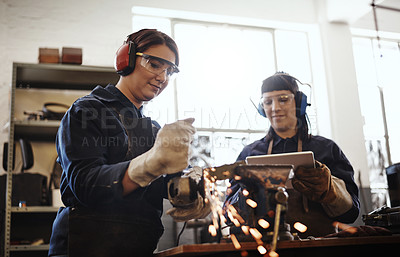 Buy stock photo Cropped shot of two attractive young female artisans using an angle grinder in their workshop