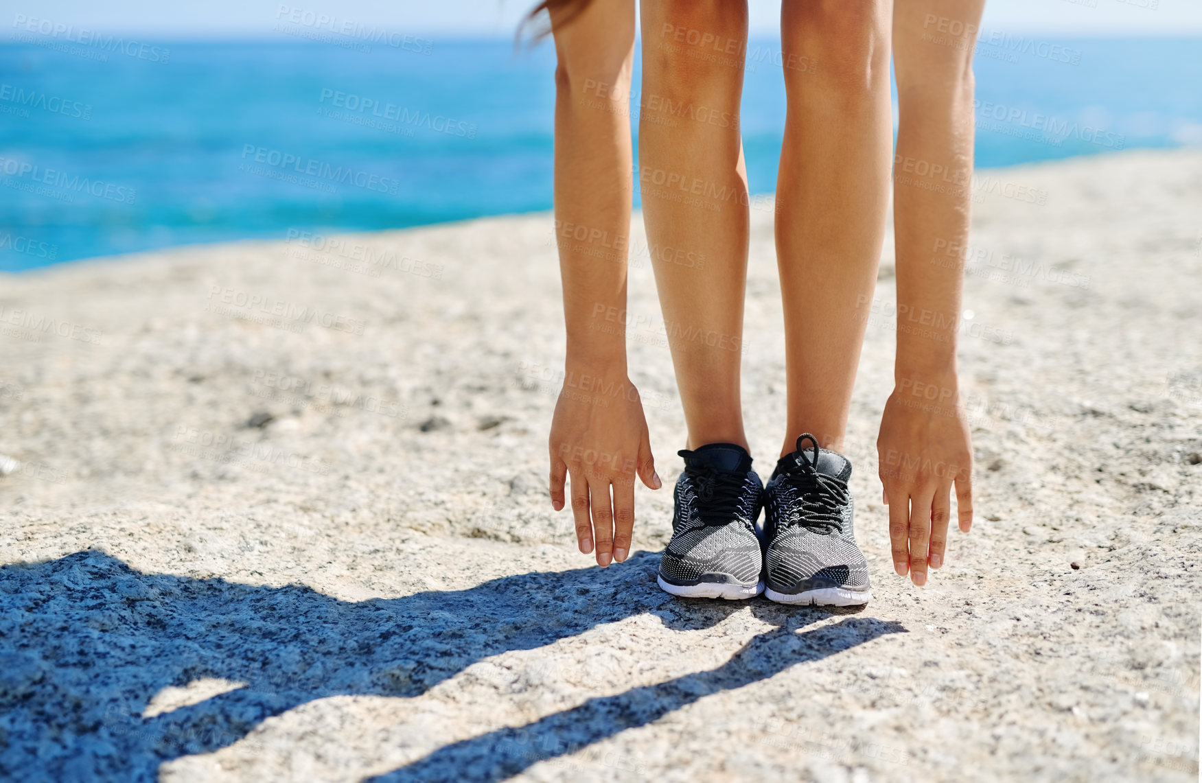 Buy stock photo Woman, shoes and stretching with hands on beach for fitness, exercise or warm up on rock in nature. Female person, legs or reaching for toes, workout or yoga in pilates or balance by ocean coast