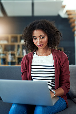 Buy stock photo Shot of a young woman using a laptop while relaxing on the sofa at home