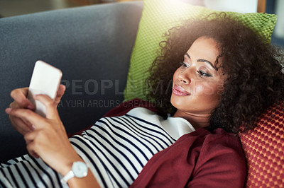 Buy stock photo Shot of a young woman using a mobile phone while relaxing on the sofa at home