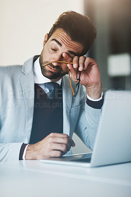 Buy stock photo Shot of a young businessman looking exhausted while working on a laptop in an office